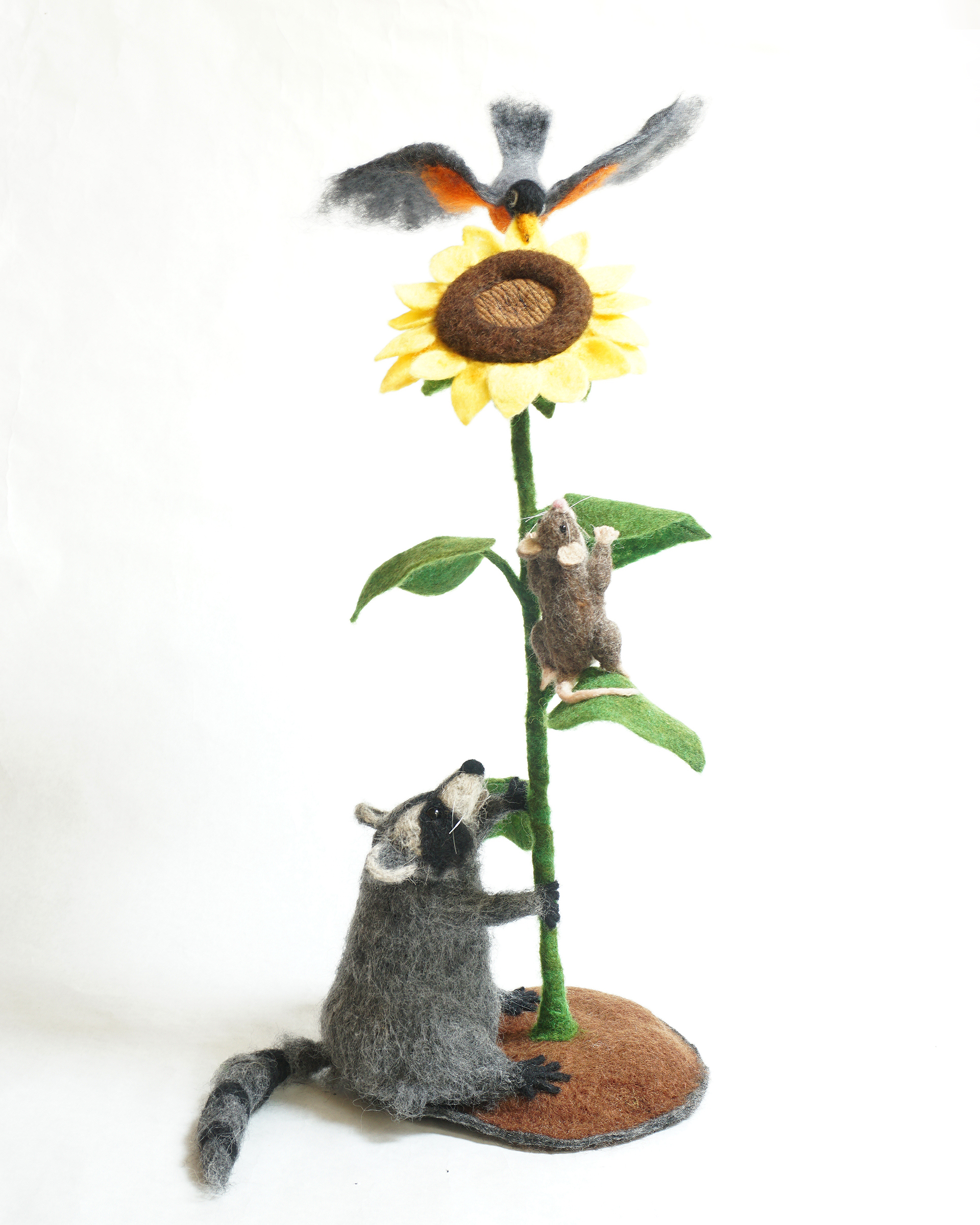 Helping Sunflower is needle felted wool sculpture over a wire and quilt batting armature form. Anthropomorphic raccoon, mouse and robin work together to help a sunflower