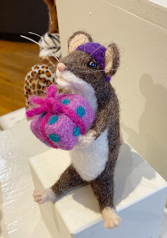 For You is an anthropomorphic mouse holding a brightly wrapped gift and wearing a purple hat