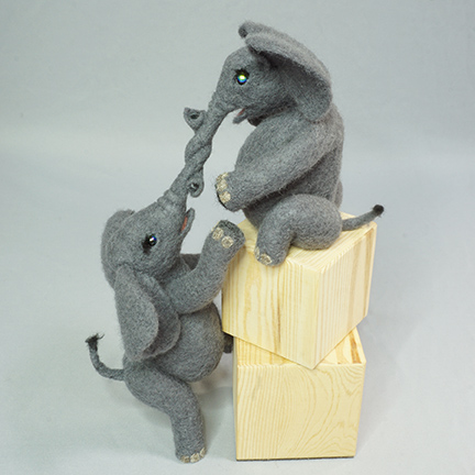 two young elephants helping each other climb blocks. Needlefelted sculpture on wooden blocks