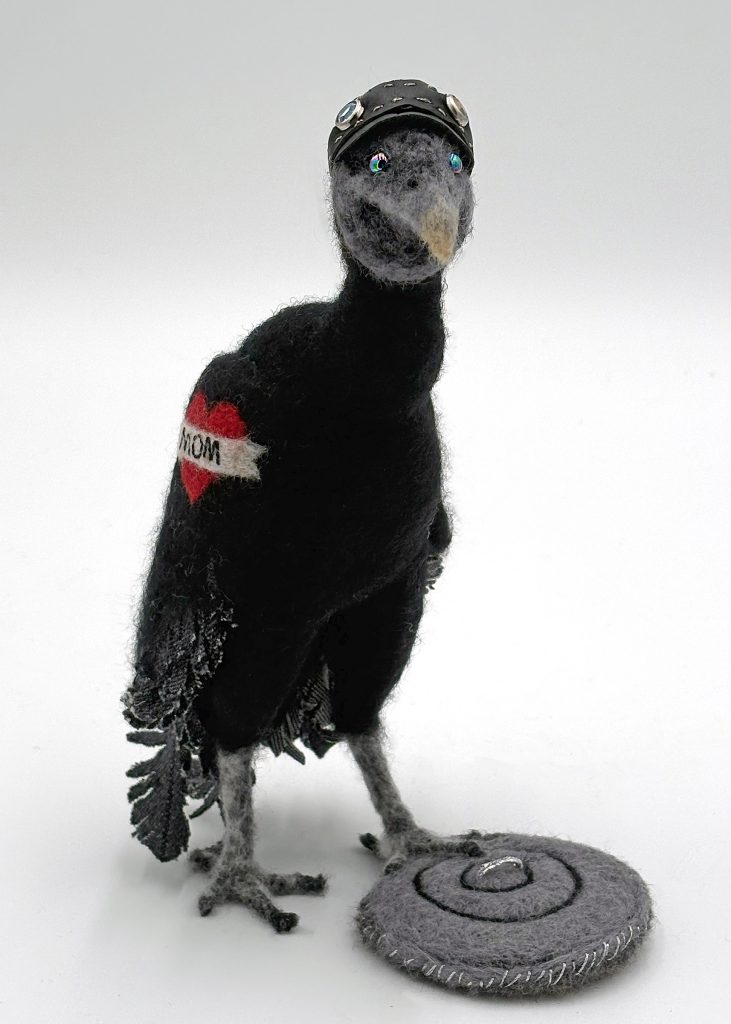 Hillsborough Hooligan needle felted black vulture with hand sewn cap of recycled black leather, red heart/mom tattoo, shredded denim tail and wing feathers, stands on a trashcan lid