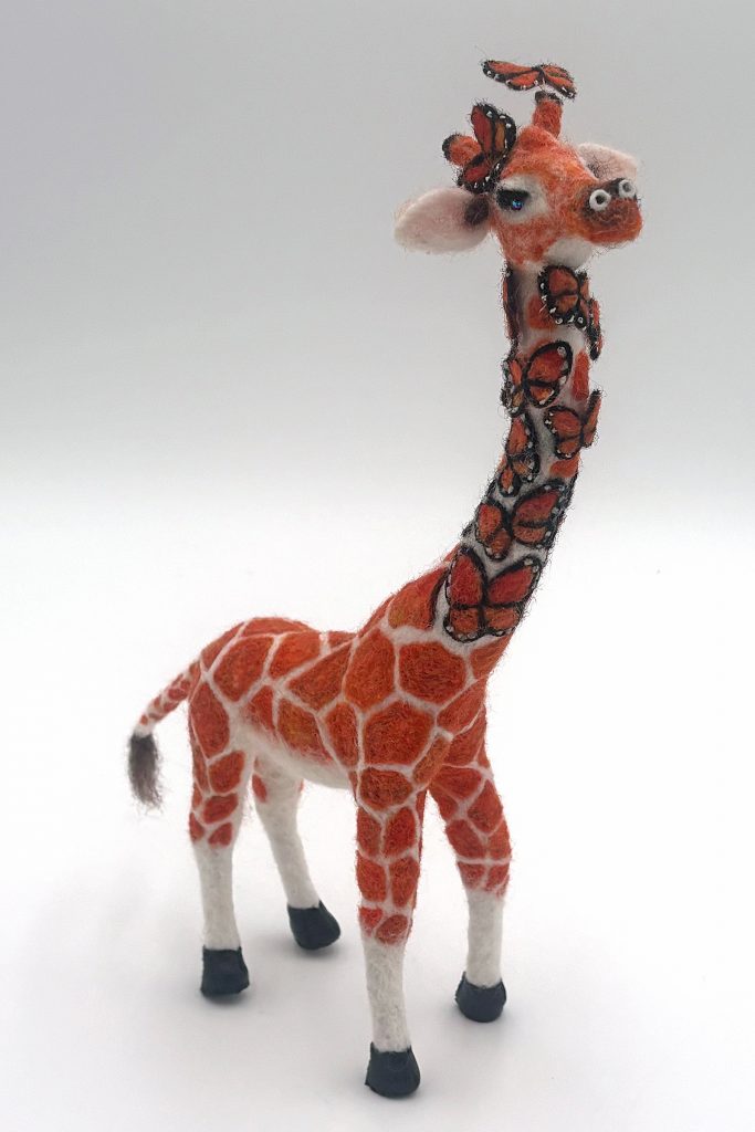 Needle felted giraffe sculpture by Lynn Wartski . Natural white and orange giraffe with coat pattern that morphs into butterflies 