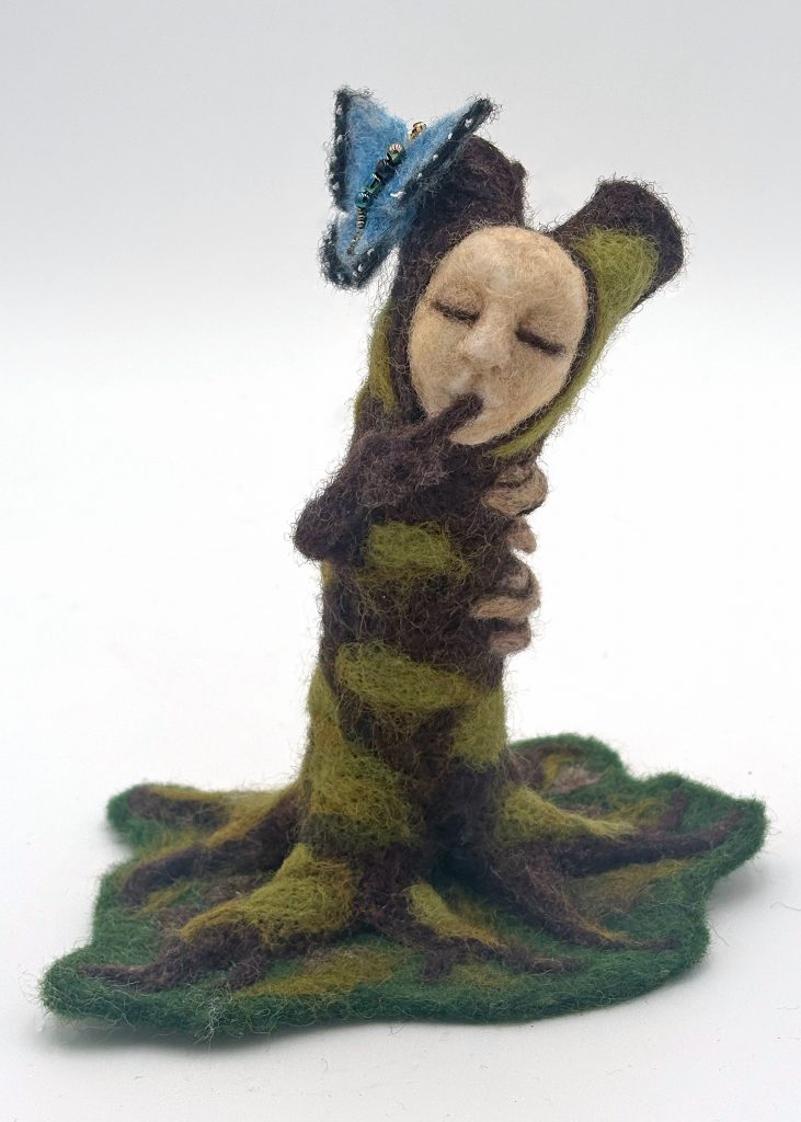 Needle felted wood spirit sculpture by Lynn Wartski. Brown trunk with green moss and shelf mushrooms.  natural tan face fith branch "arm" making "shhhh" gestures.  A blue and black butterfly sits on top