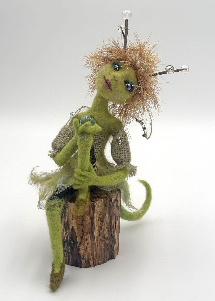 Dew needle felted mythical figure sculpture by Lynn Wartski. Seated figure in green with natural wood antennae with blown glass finials. Special yarn hair, and burlap dress detail. figure is seated on a natural wood "stump" base.
