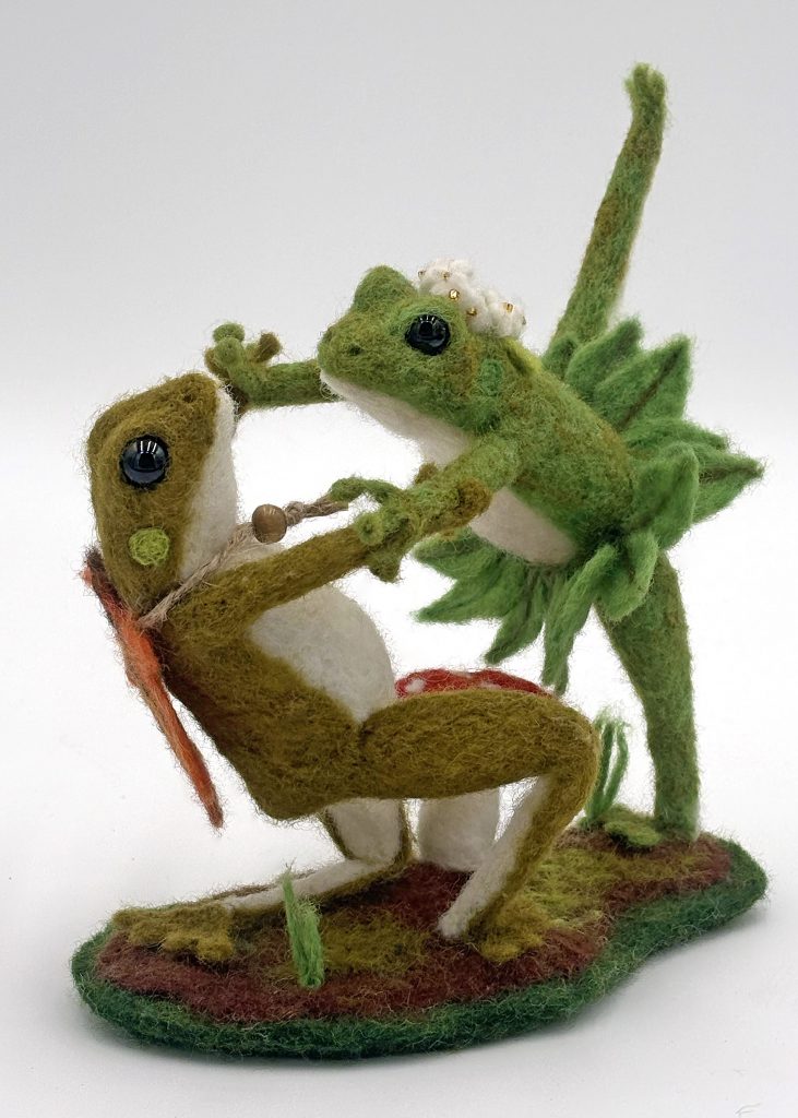 needle felted pair of ballet dancing frogs.  Green and natural color frogs. Kneeling figure weaars a fall leaf cape, standing frog with one leg up has green leaf tutu, and white flower crown.