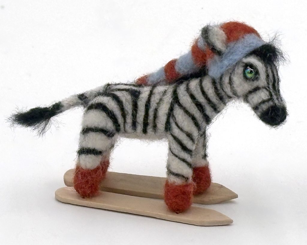 needle felted one-of-a-kind holiday ornament by Lynn Wartski. Zebra on craft stick skis, blue and red hat and red boots